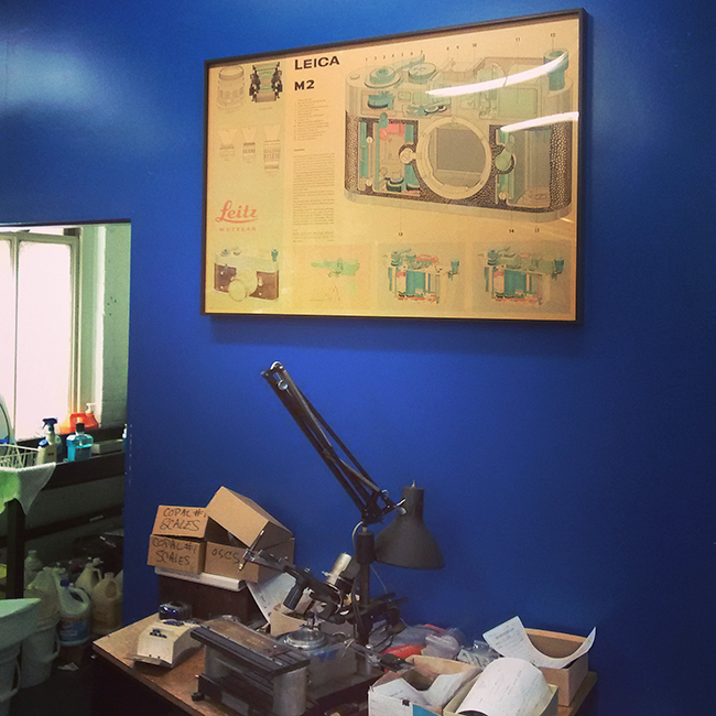 A Leica M2 poster hangs on a deep-blue wall above Steve Grime’s custom made engraving tool, used to make custom aperture and shutter-speed scales.